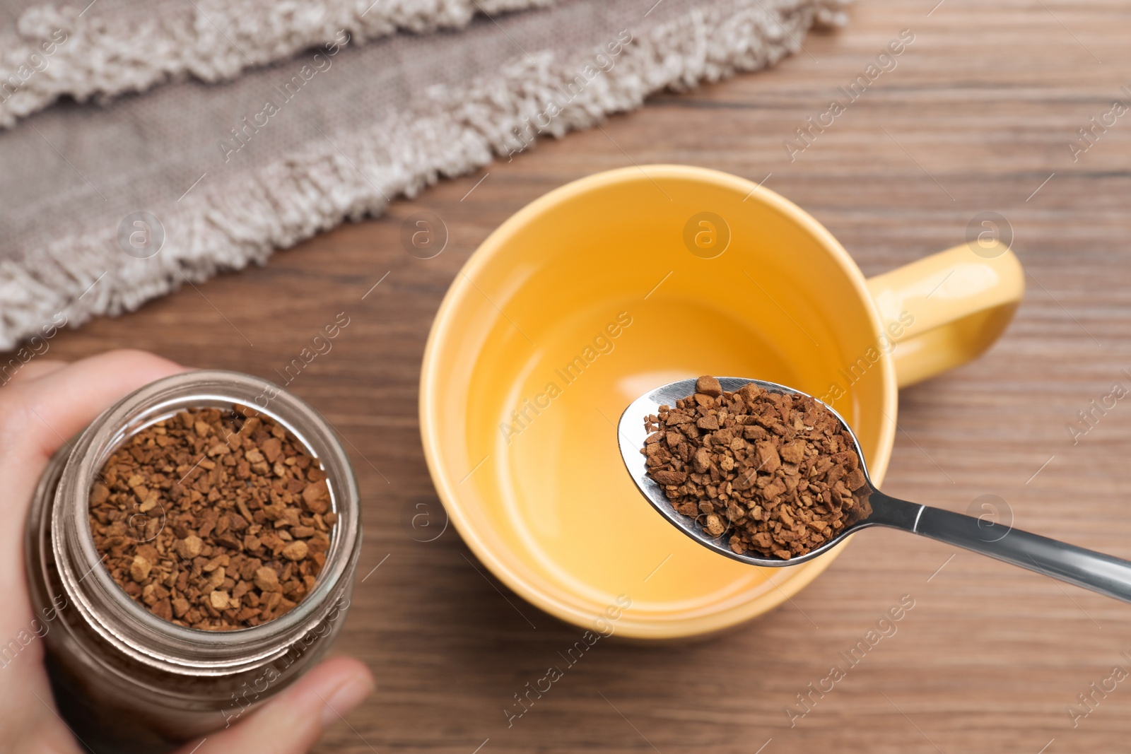 Photo of Woman pouring instant coffee into cup at wooden table, top view