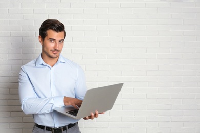 Young male teacher with laptop near brick wall. Space for text