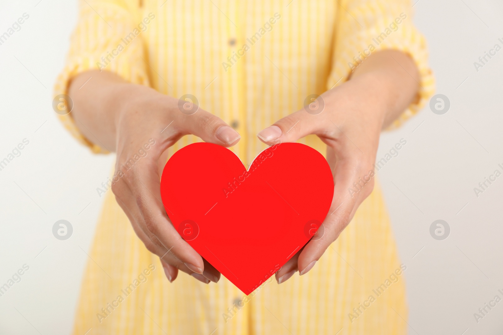 Photo of Young woman holding red heart on light background, closeup