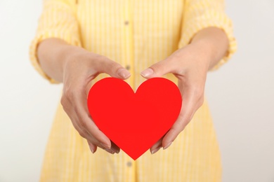 Young woman holding red heart on light background, closeup