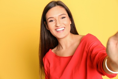 Young beautiful woman taking selfie against color background