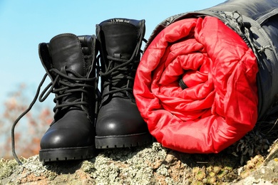 Photo of Boots and sleeping bag on rock outdoors. Camping equipment