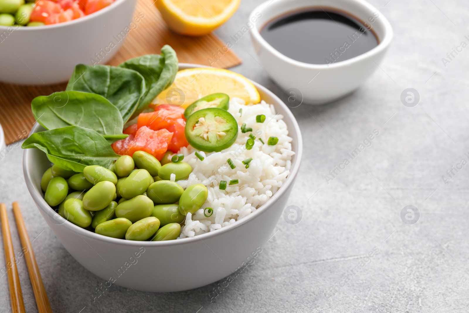 Photo of Poke bowl with salmon, edamame beans and rice on light grey table. Space for text