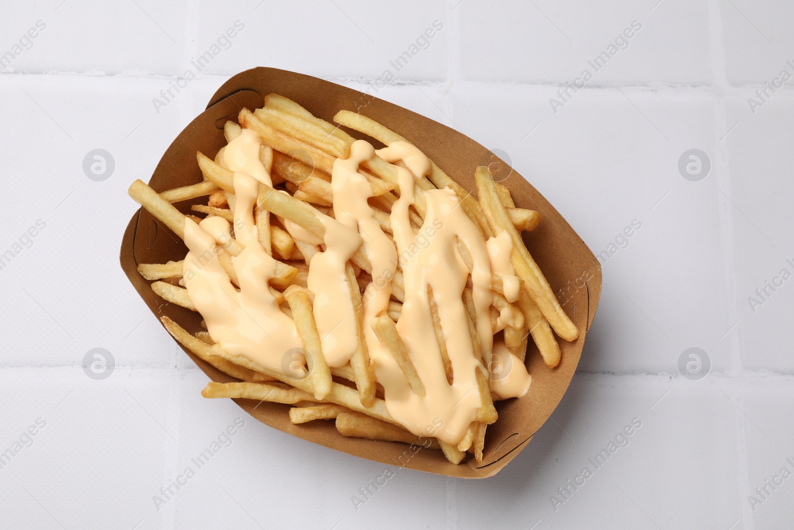 Photo of Delicious French fries with cheese sauce on white tiled table, top view