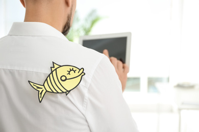 Photo of Man with paper fish on back indoors, closeup. April fool's day