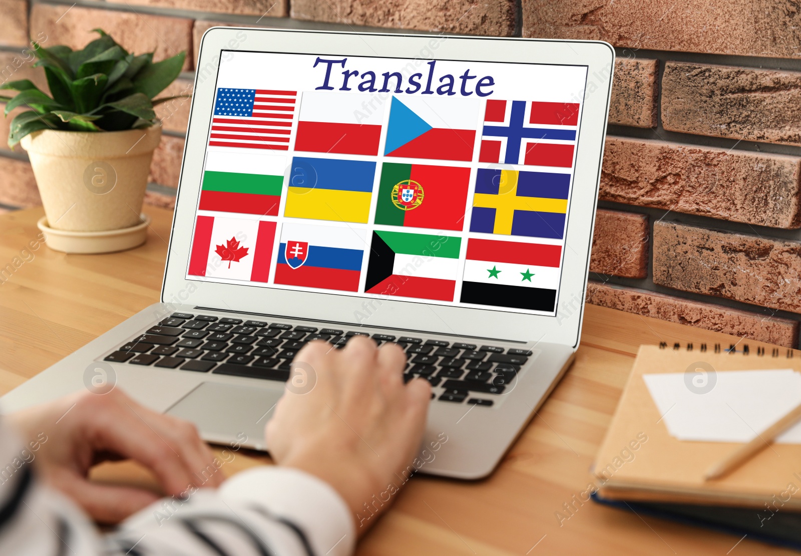 Image of Translator using modern laptop with images of different flags on screen at table indoors, closeup