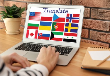 Image of Translator using modern laptop with images of different flags on screen at table indoors, closeup