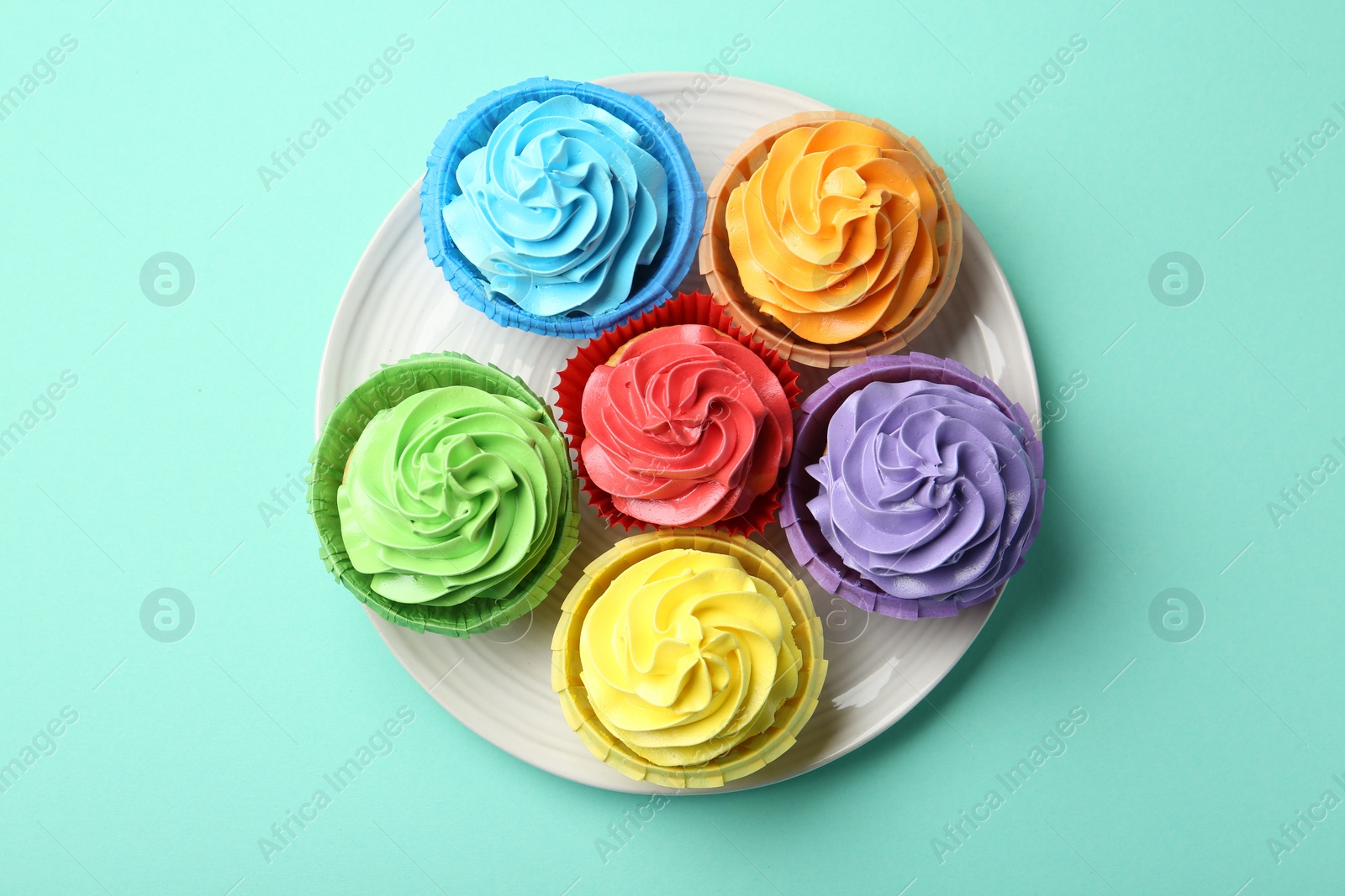 Photo of Plate with delicious bright cupcakes on turquoise background, top view