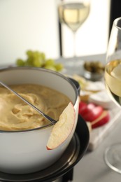 Fork with piece of apple and melted cheese in fondue pot on grey table, closeup