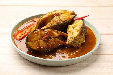 Photo of Tasty fish curry on white wooden table, closeup. Indian cuisine