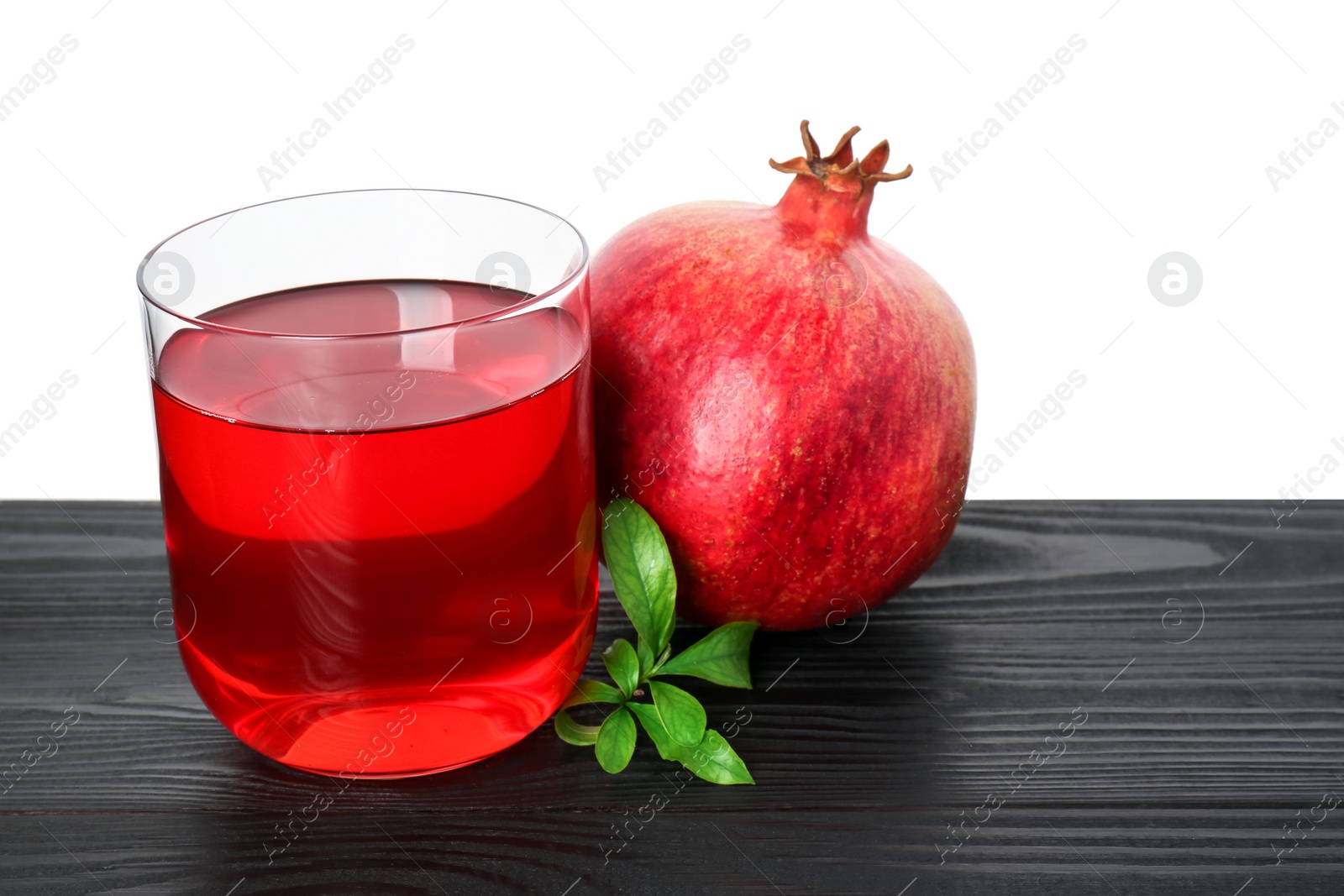 Photo of Refreshing pomegranate juice in glass, leaves and fruit on black wooden table against white background