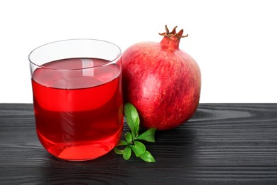 Photo of Refreshing pomegranate juice in glass, leaves and fruit on black wooden table against white background