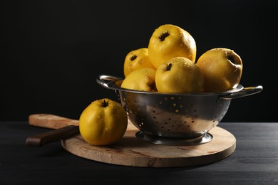 Photo of Tasty ripe quinces with water drops in metal colander and knife on black wooden table