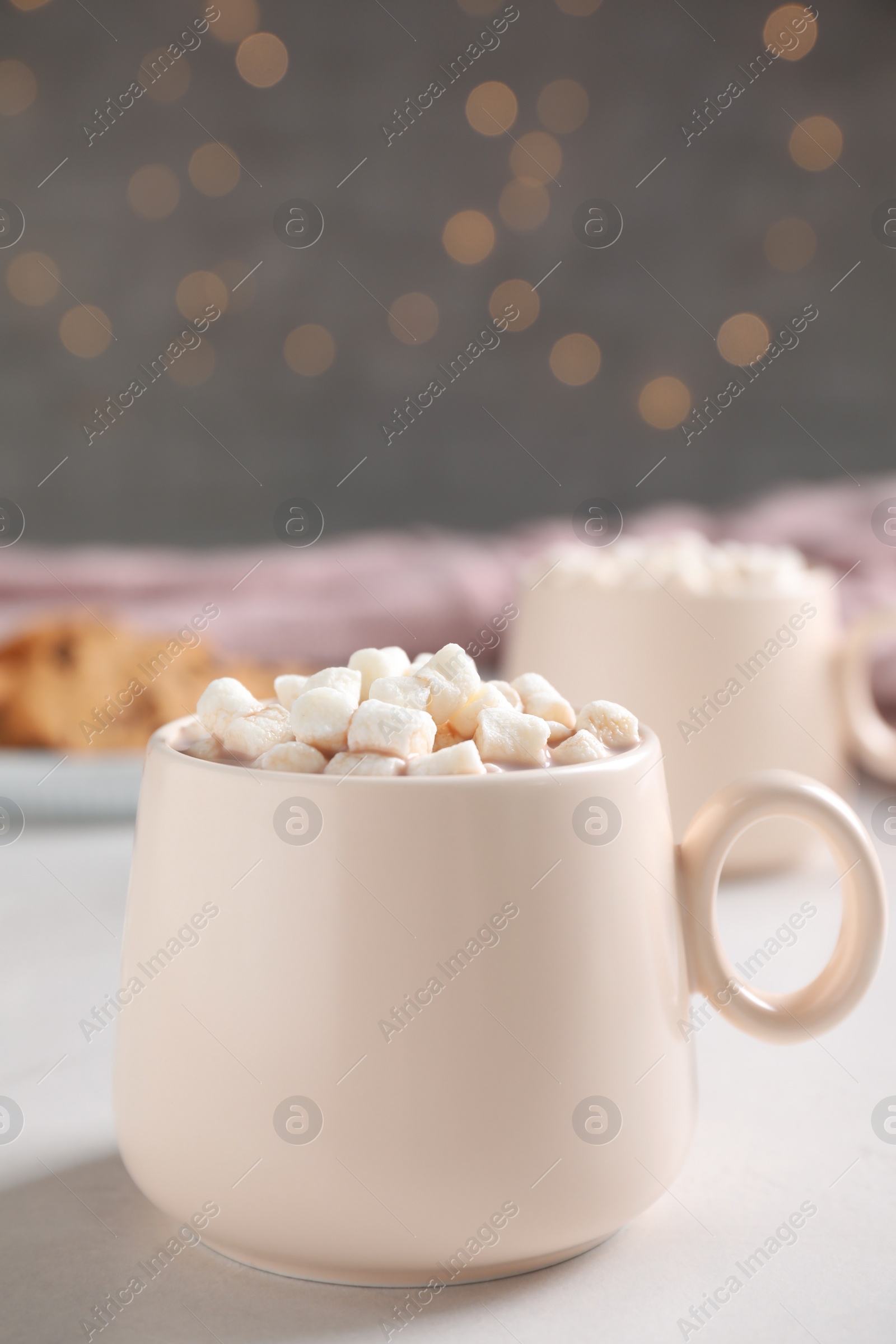 Photo of Cup of delicious hot cocoa with marshmallows on white table against blurred lights