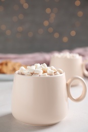 Cup of delicious hot cocoa with marshmallows on white table against blurred lights