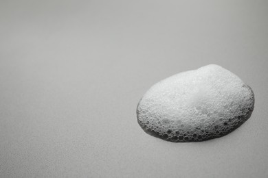 Photo of Drop of fluffy soap foam on grey background. Space for text