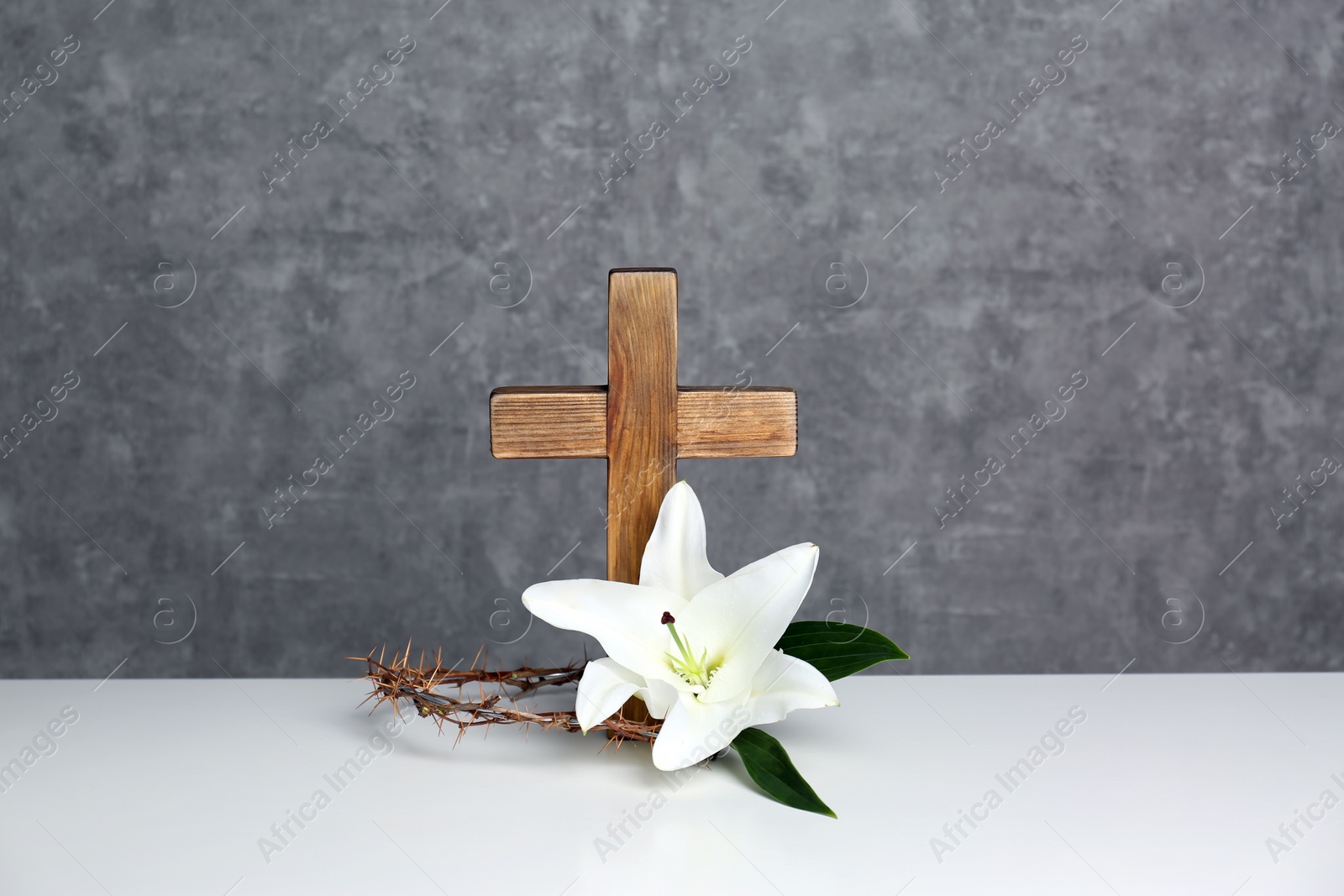 Photo of Wooden cross, crown of thorns and blossom lily on table against color background