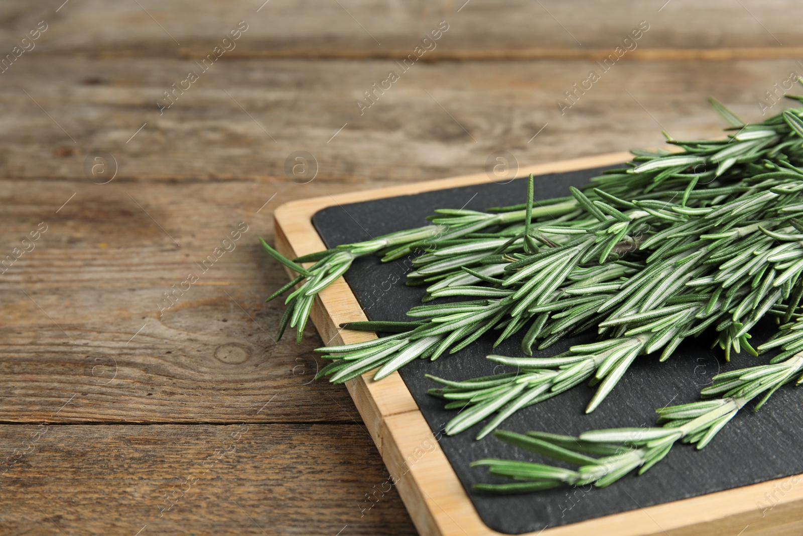 Photo of Board with fresh rosemary twigs on wooden table, closeup. Space for text