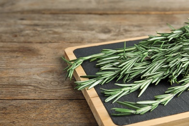 Photo of Board with fresh rosemary twigs on wooden table, closeup. Space for text