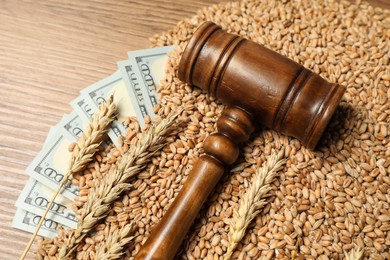 Dollar banknotes, judge's gavel, wheat ears and grains on wooden table, closeup. Agricultural business