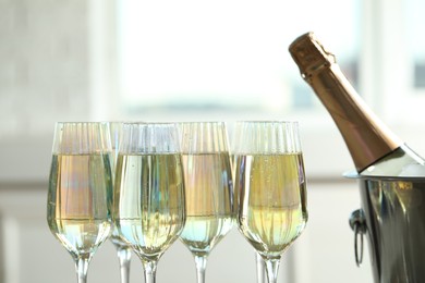 Photo of Glasses of champagne and ice bucket with bottle on blurred background