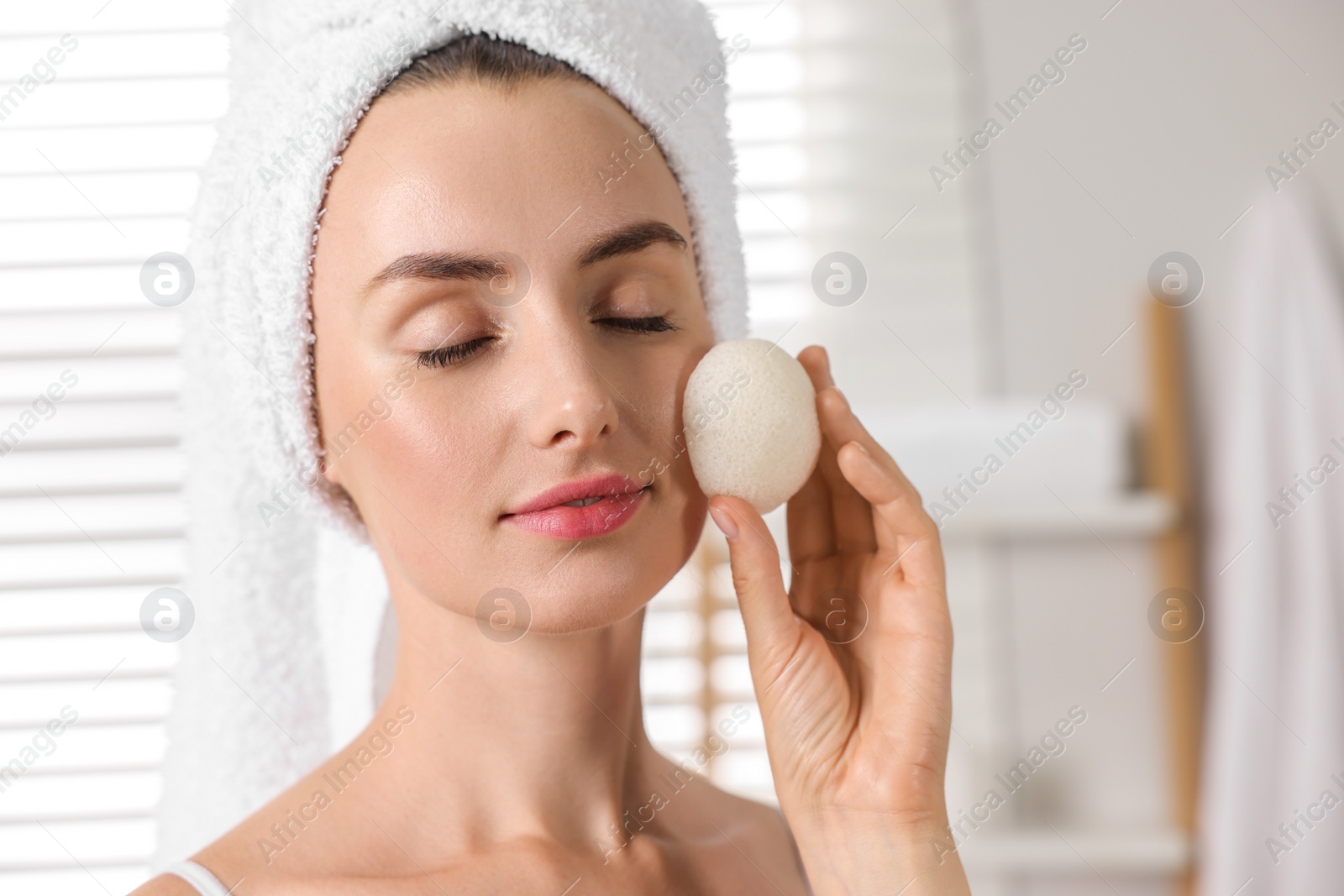 Photo of Happy young woman washing her face with sponge in bathroom