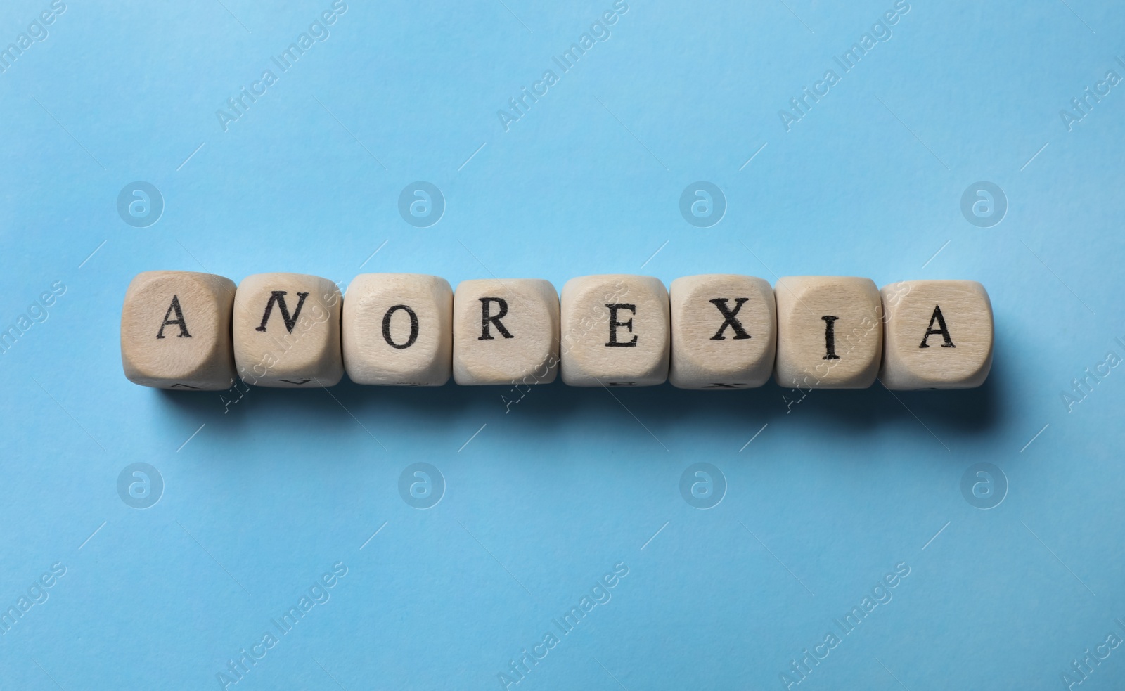 Photo of Word Anorexia made of wooden cubes on light blue background, flat lay