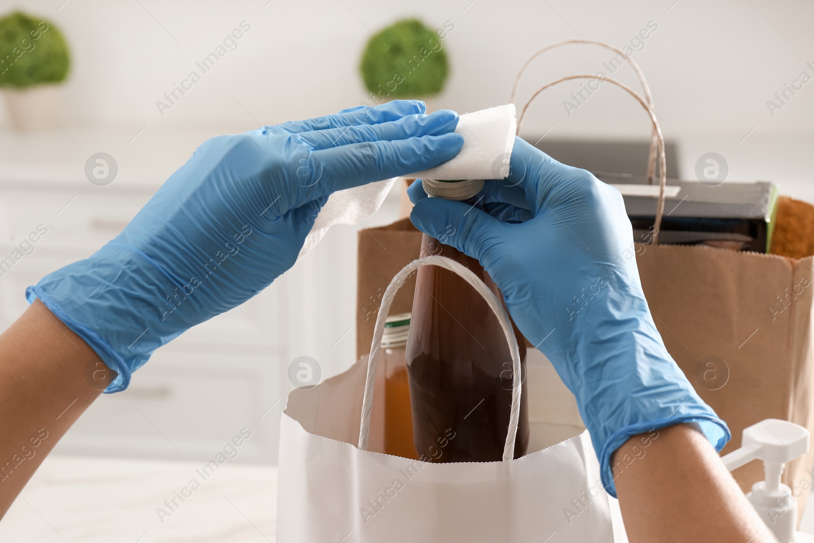 Photo of Woman cleaning newly purchased bottle of juice with antiseptic wipe indoors, closeup. Preventive measures during COVID-19 pandemic