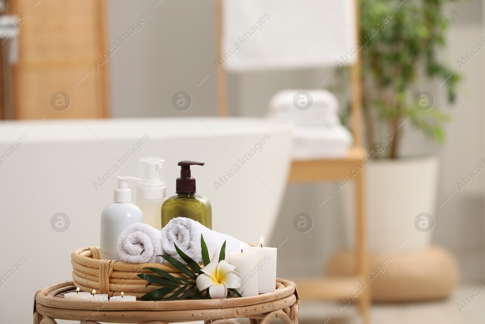 Photo of Spa products, burning candles, plumeria flower and tropical leaf on table in bathroom. Space for text