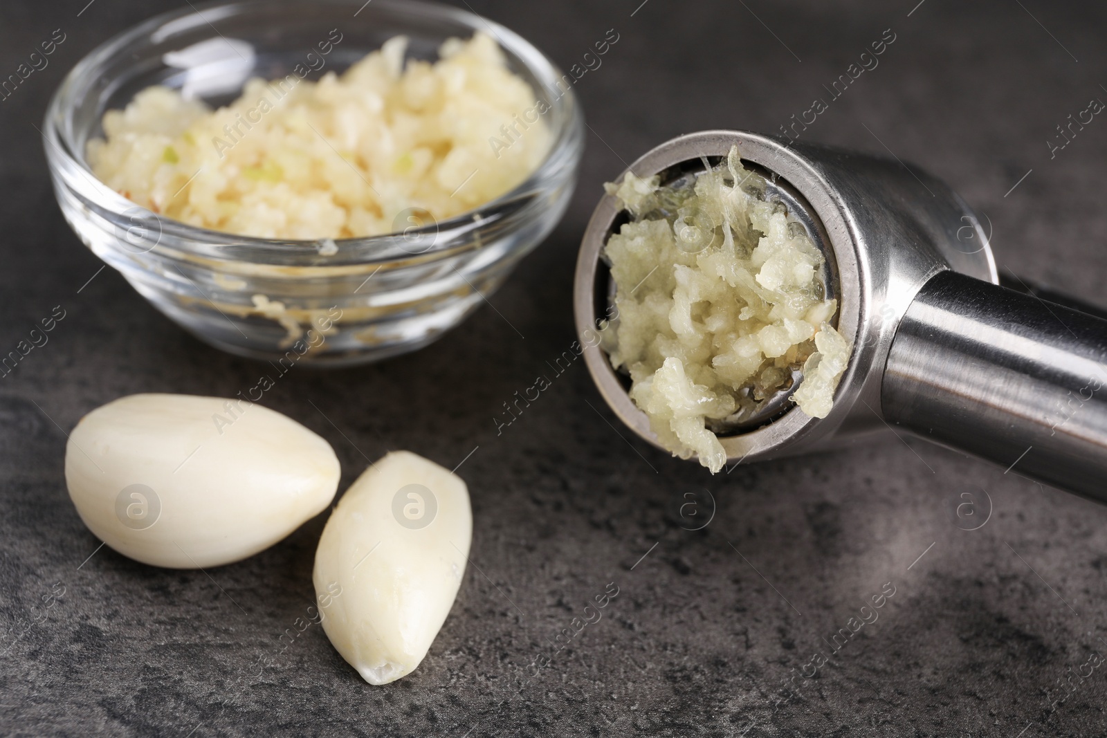 Photo of Garlic press, cloves and mince on grey table, closeup