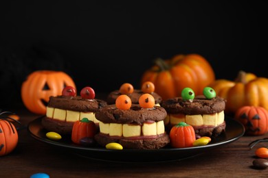 Photo of Delicious desserts decorated as monsters on wooden table. Halloween treat