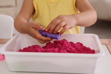 Little girl playing with bright kinetic sand at table indoors, closeup