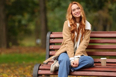 Photo of Portrait of smiling woman sitting on bench in autumn park. Space for text