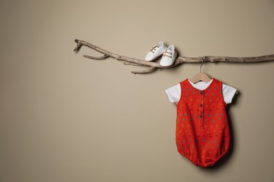 Photo of Baby bodysuit and booties on decorative branch near beige wall. Space for text