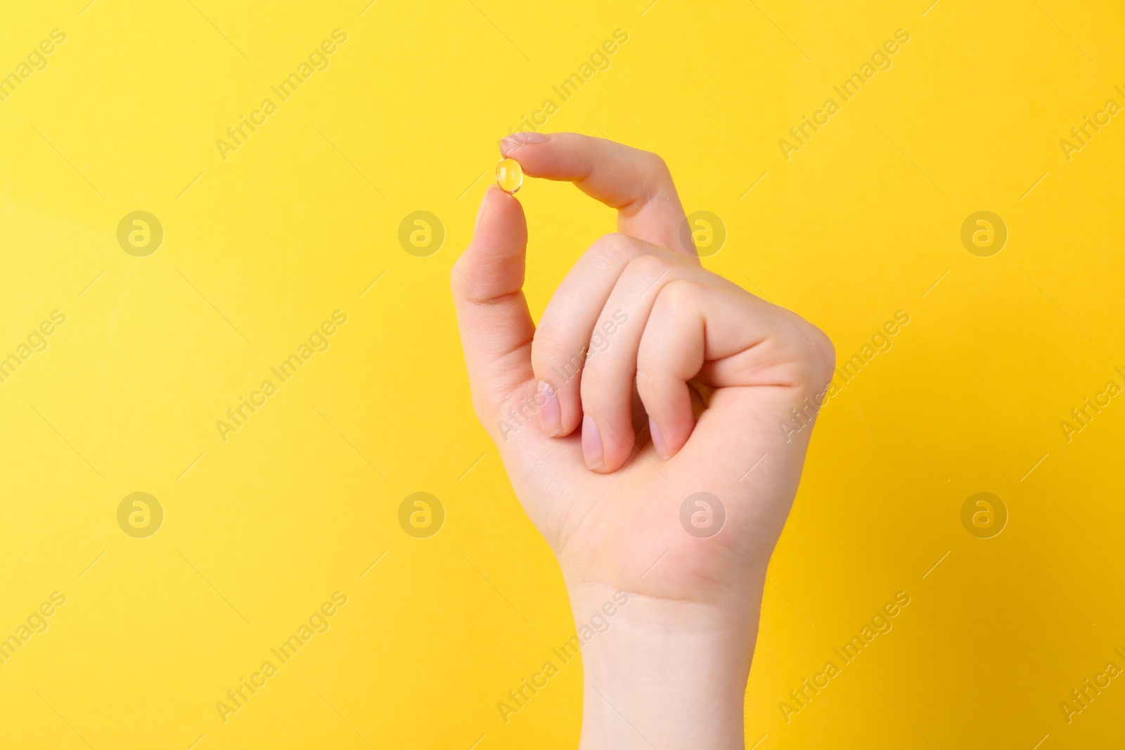 Photo of Woman holding vitamin capsule on yellow background, closeup. Space for text