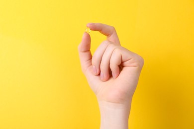 Woman holding vitamin capsule on yellow background, closeup. Space for text