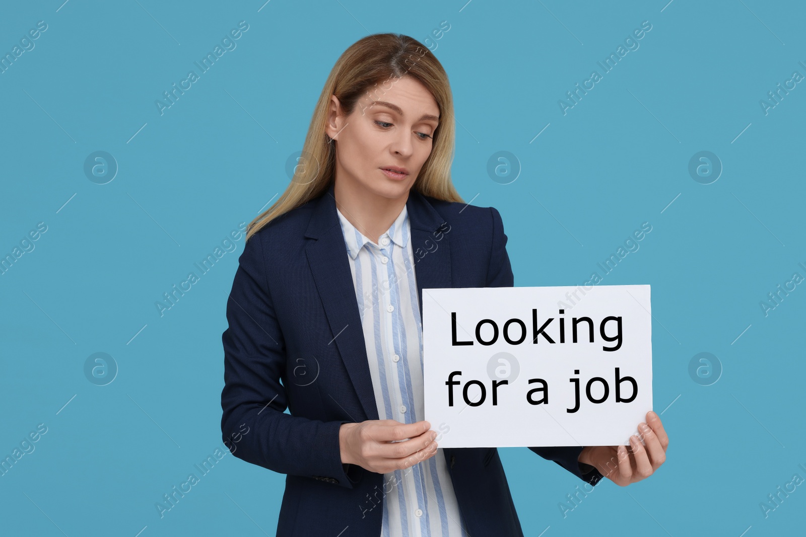 Photo of Unemployed woman holding sign with phrase Looking For A Job on light blue background