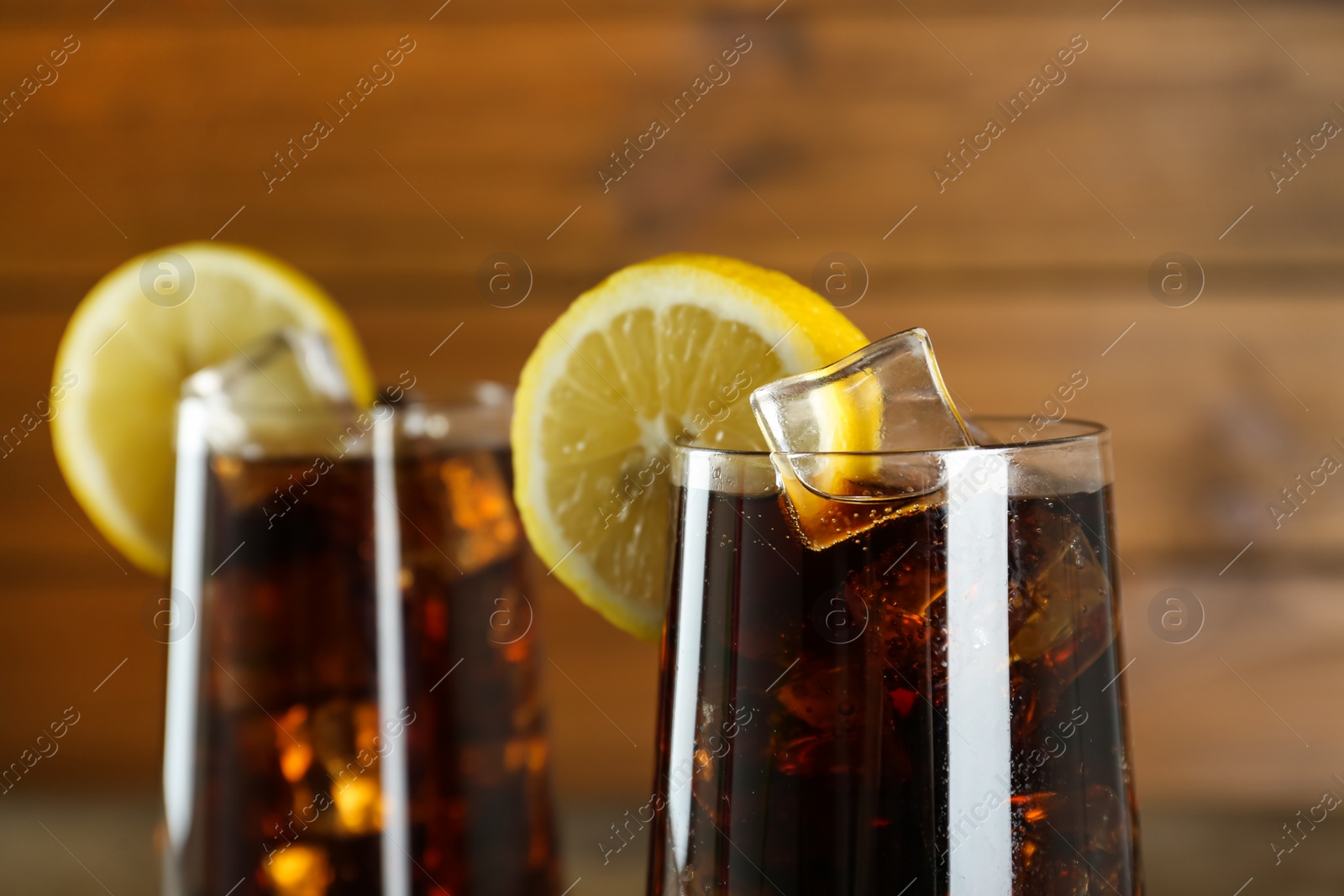 Photo of Glasses of refreshing soda water with ice cubes and lemon slices on blurred background, closeup