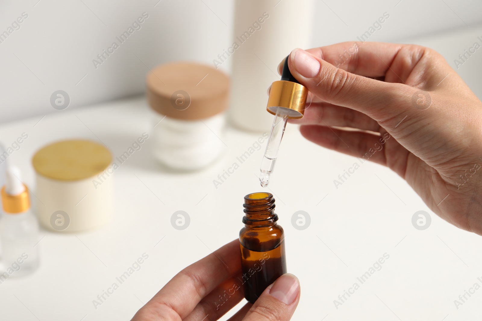 Photo of Woman with bottle of cosmetic serum and pipette at white table, closeup