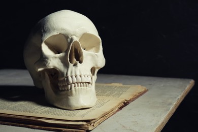 Photo of Human skull and old book on table against black background, space for text