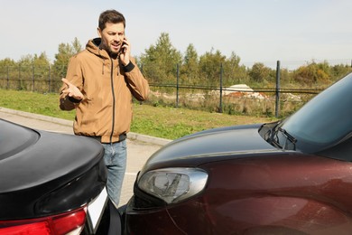 Photo of Man talking on phone near car with scratch outdoors Auto accident