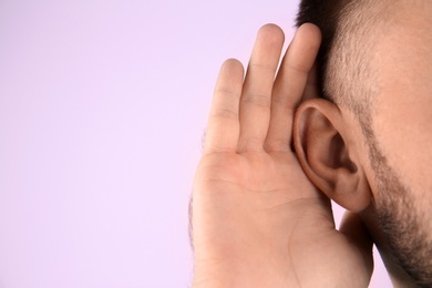Photo of Young man with hearing problem on color background with copy space text, closeup