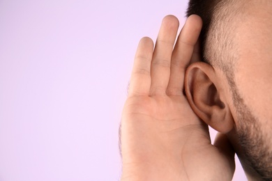 Young man with hearing problem on color background with copy space text, closeup