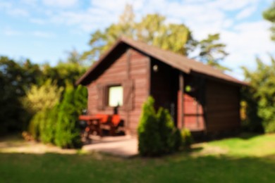 Photo of Cozy wooden house surrounded by lush nature on sunny day, blurred view