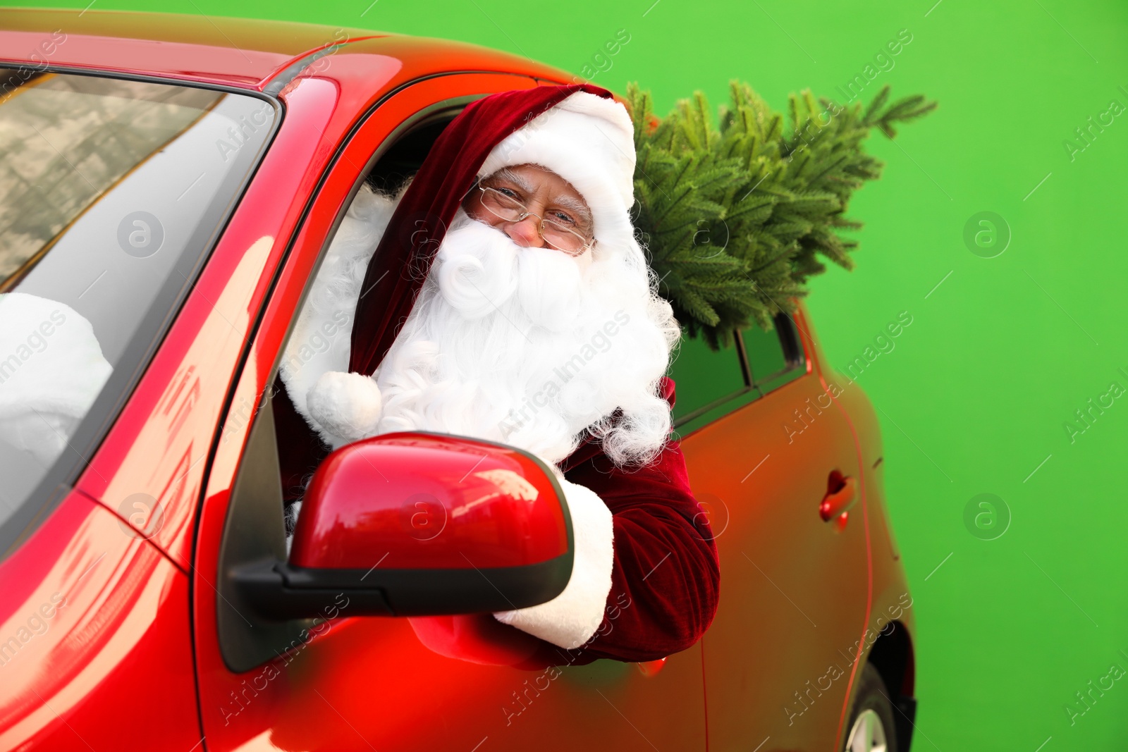 Photo of Authentic Santa Claus with fir tree driving car against green background