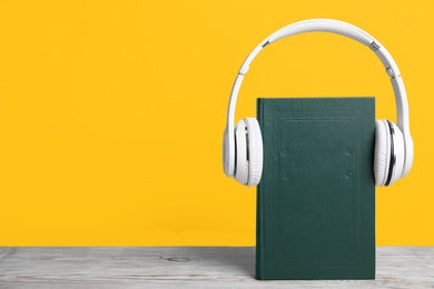 Photo of Book and modern headphones on white wooden table against yellow background. Space for text