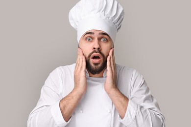 Photo of Surprised young chef in uniform on grey background