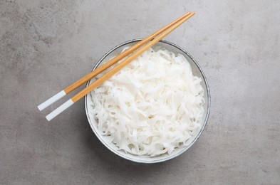 Photo of Bowl with cooked rice noodles and chopsticks on light grey table, top view