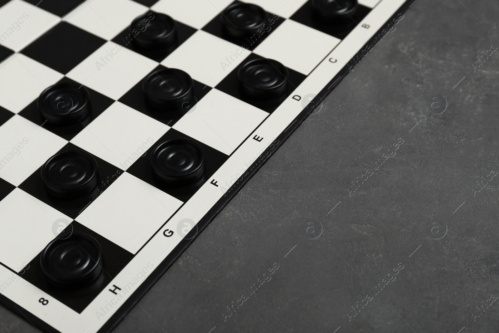 Photo of Checkerboard with game pieces on grey table, closeup. Space for text