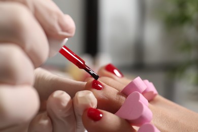 Photo of Pedicurist painting client`s toenails with red polish in beauty salon, closeup